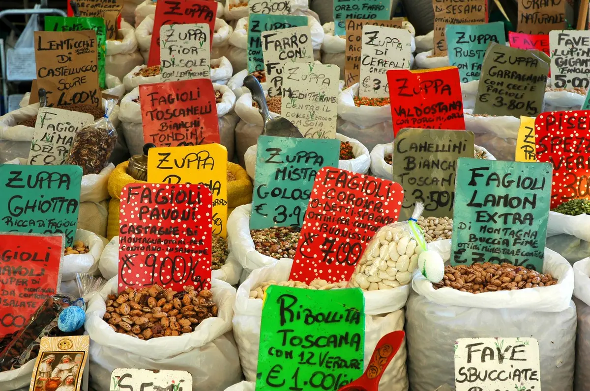 Open sacks of assorted dried beans and lentils in reds, browns, and creams at a market.